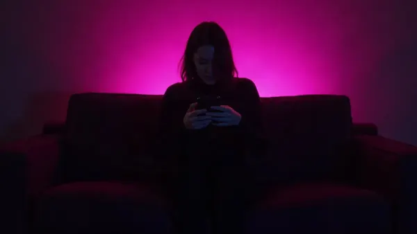 Silhouette von hinten auf einem Sofa mit Handy in einem dunklen Raum mit magentafarbenem Schein (Illustration zum Artikel)